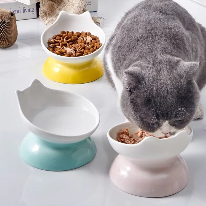Katze frisst aus einem erhöhten Catson Neko Dish™ Keramik-Futternapf in Rosa, daneben weitere Näpfe in Blau und Gelb